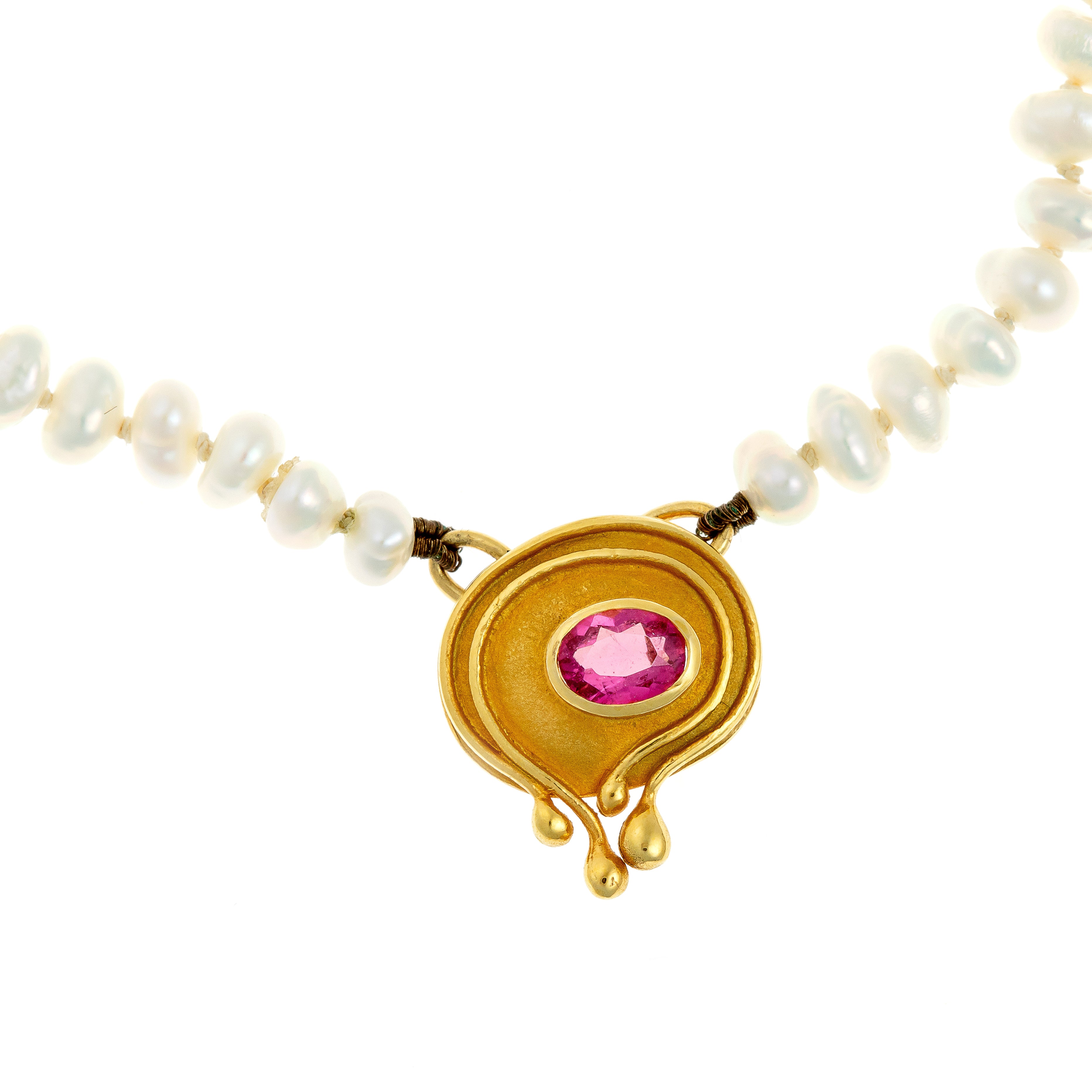 Close-up of the tourmaline pendant, highlighting the fluid gold design and bezel-set pink tourmaline.