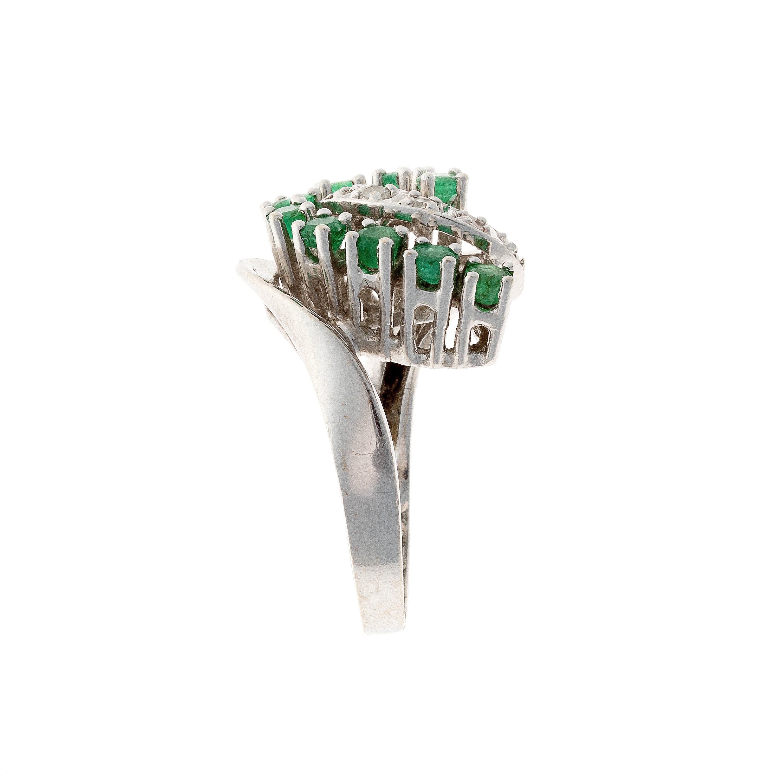 Side view of mid-century swirl cocktail ring with emeralds and diamonds in white gold.