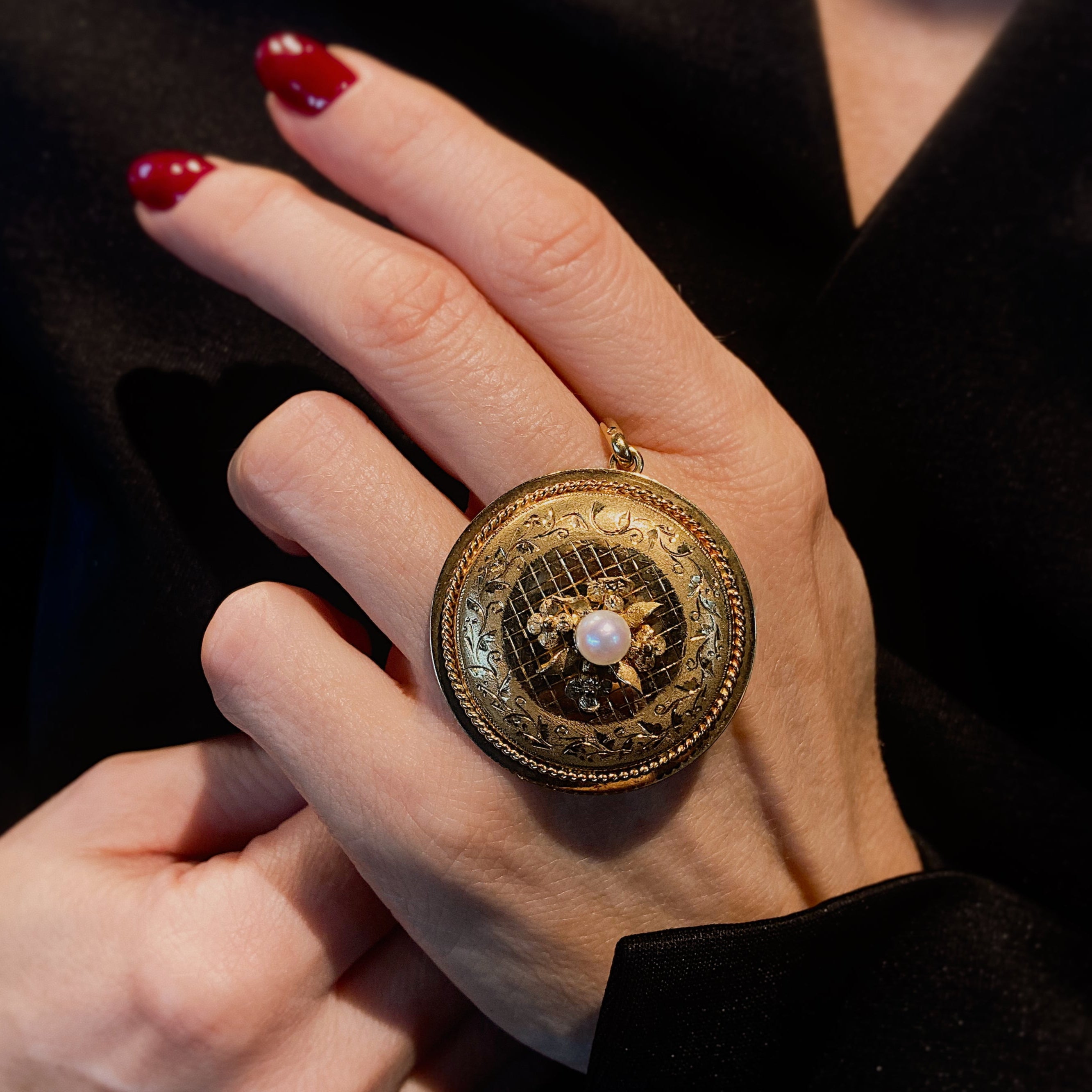 Woman model holding the antique Victorian 18K gold pendant with central cultured pearl and intricate floral repoussé detailing.