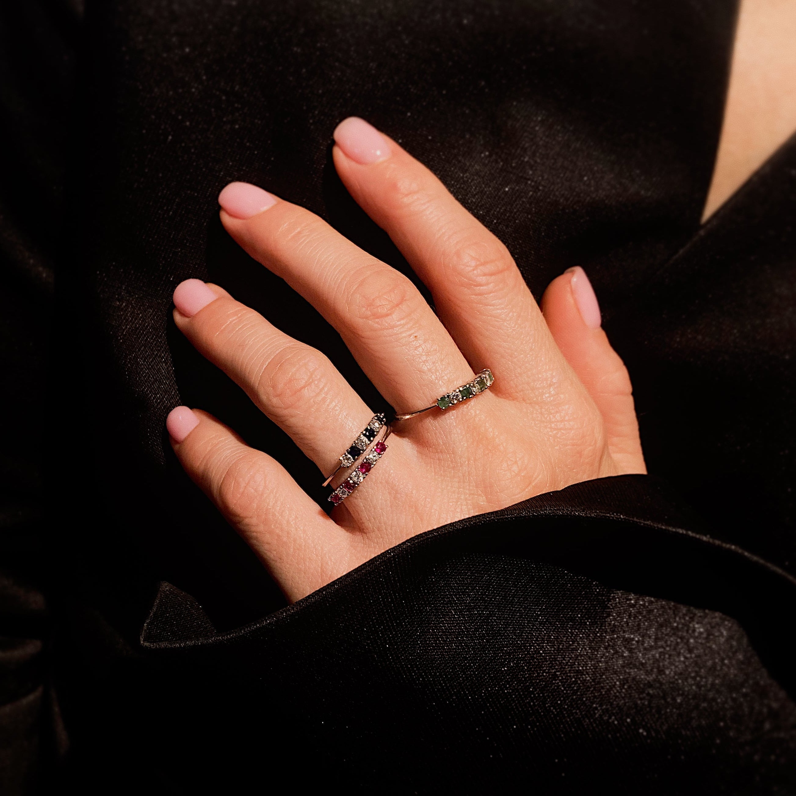 Model wearing three contemporary vintage white gold band rings with diamonds and sapphires, diamonds and rubies, and diamonds and emeralds.
