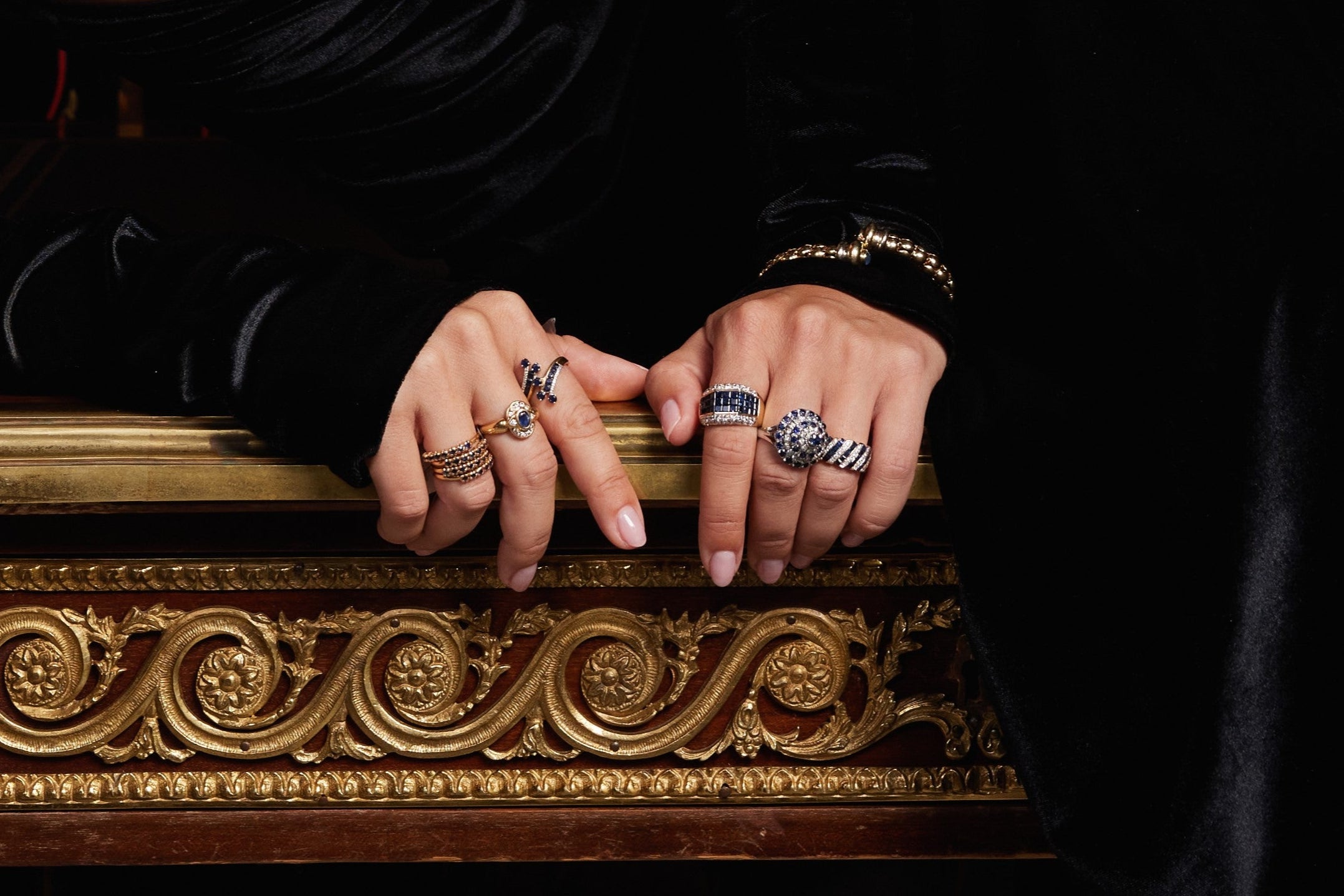Model hands wearing vintage luxury rings and holding an antique table - jewelry concierge service.