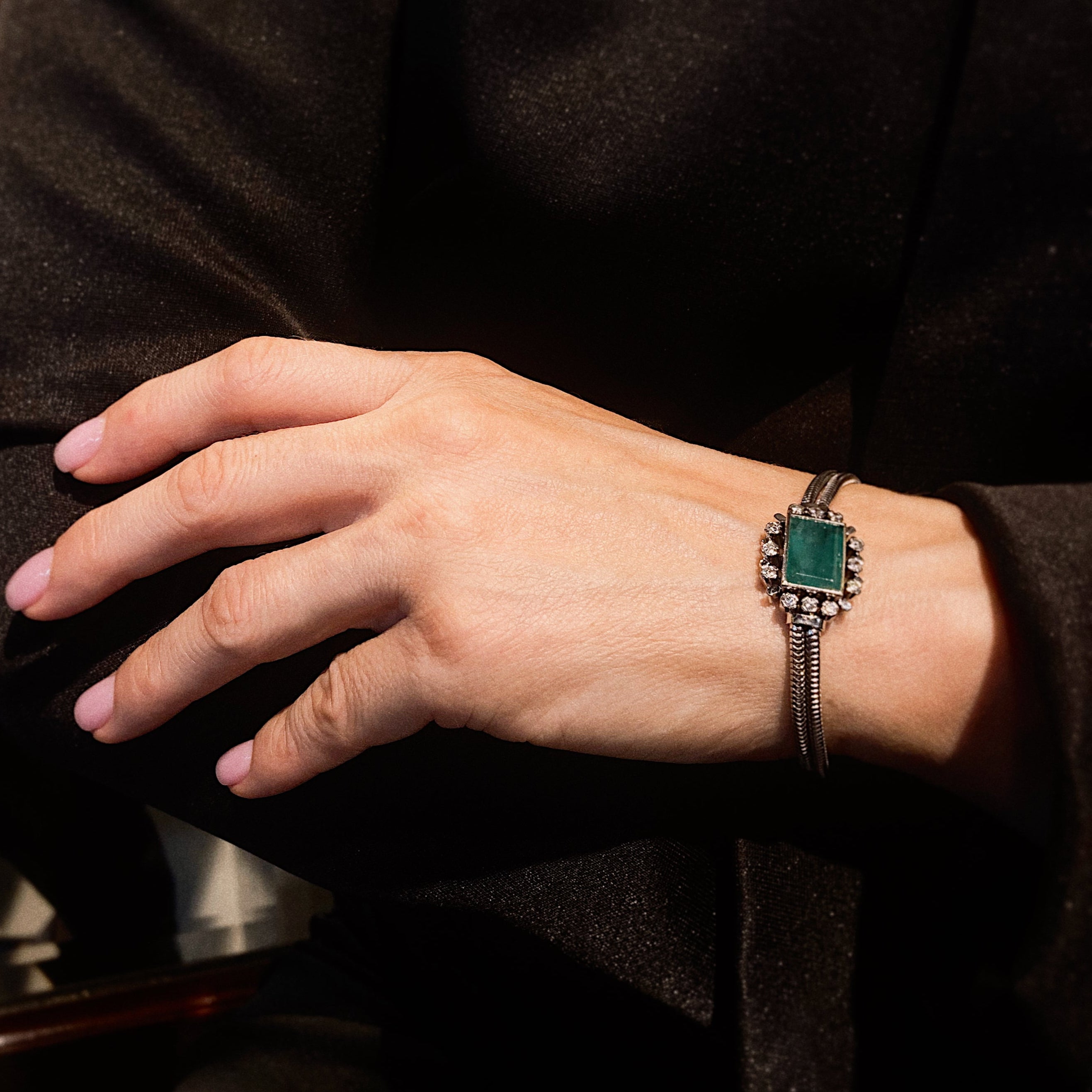 Woman model wearing the vintage mid-century French white gold bracelet with lab-grown emerald and diamonds, styled for formal chic looks.