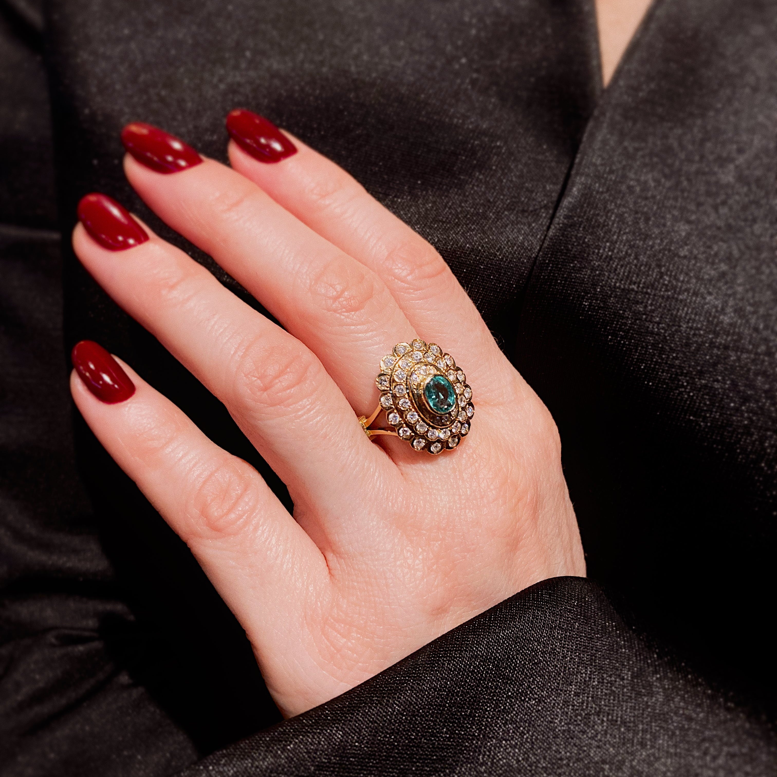 Hand einer Frau, die den Mid-Century gewellten Doppel-Halo-Cocktailring aus Gold mit Smaragd und Diamant trägt.