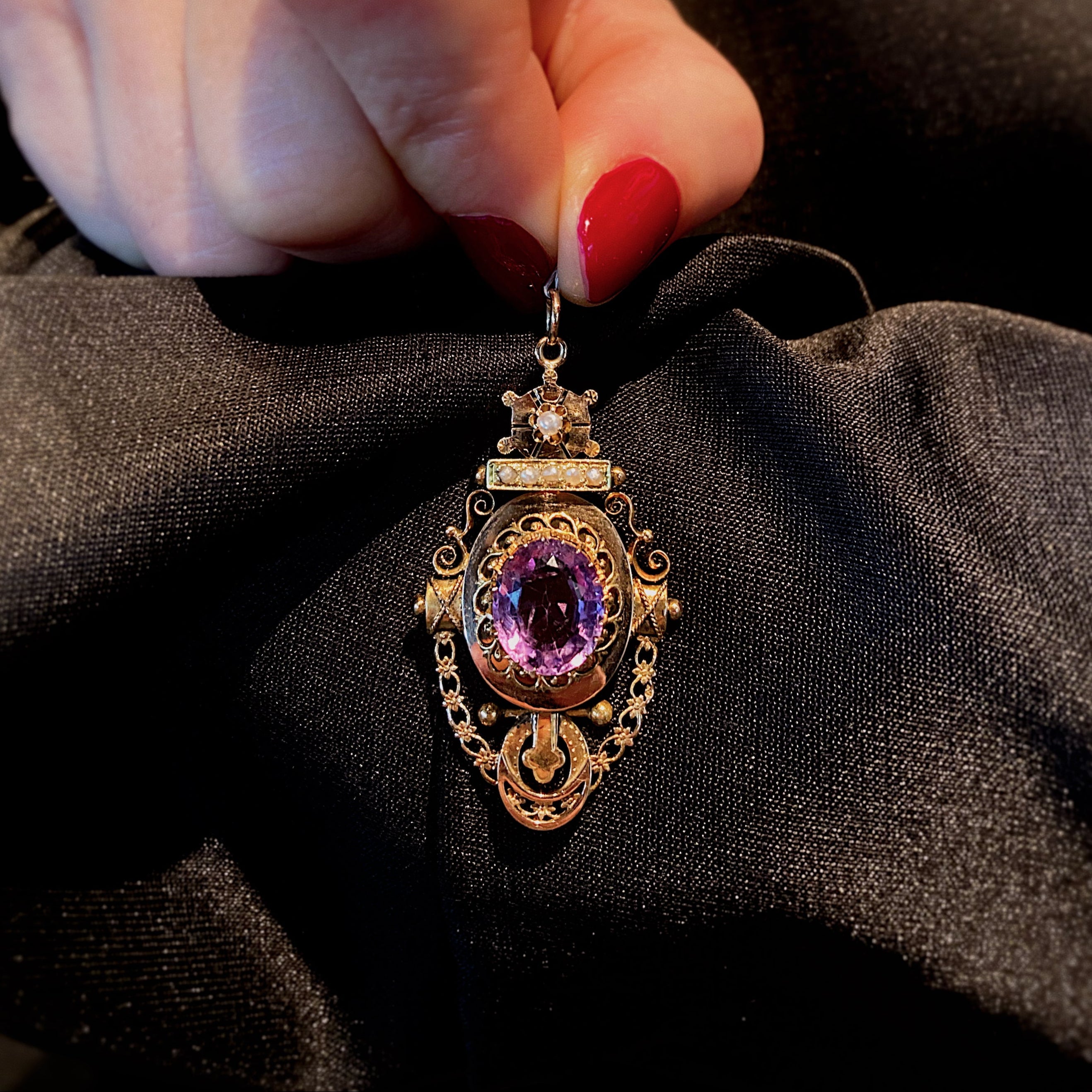Woman holding the antique Victorian Etruscan Revival gold pendant with a central amethyst and pearls.