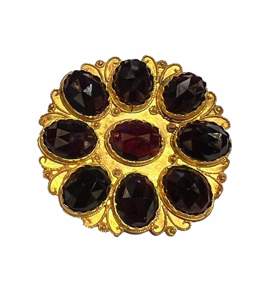A vintage 9K gold brooch featuring nine faceted garnets in a bold circular floral arrangement with scalloped gold details.