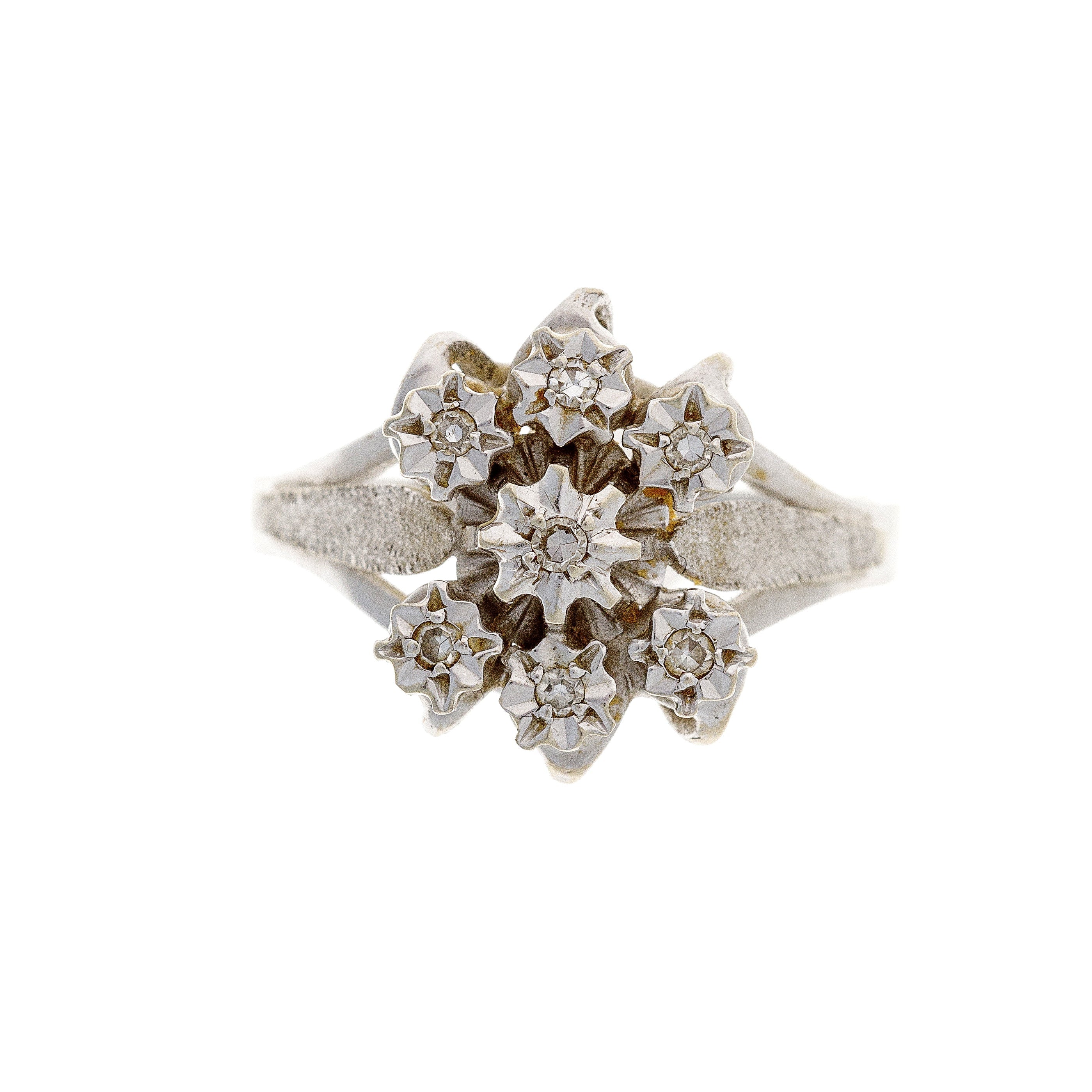 A vintage 18K white gold floral cluster ring featuring seven diamonds arranged in a delicate flower-inspired design.
