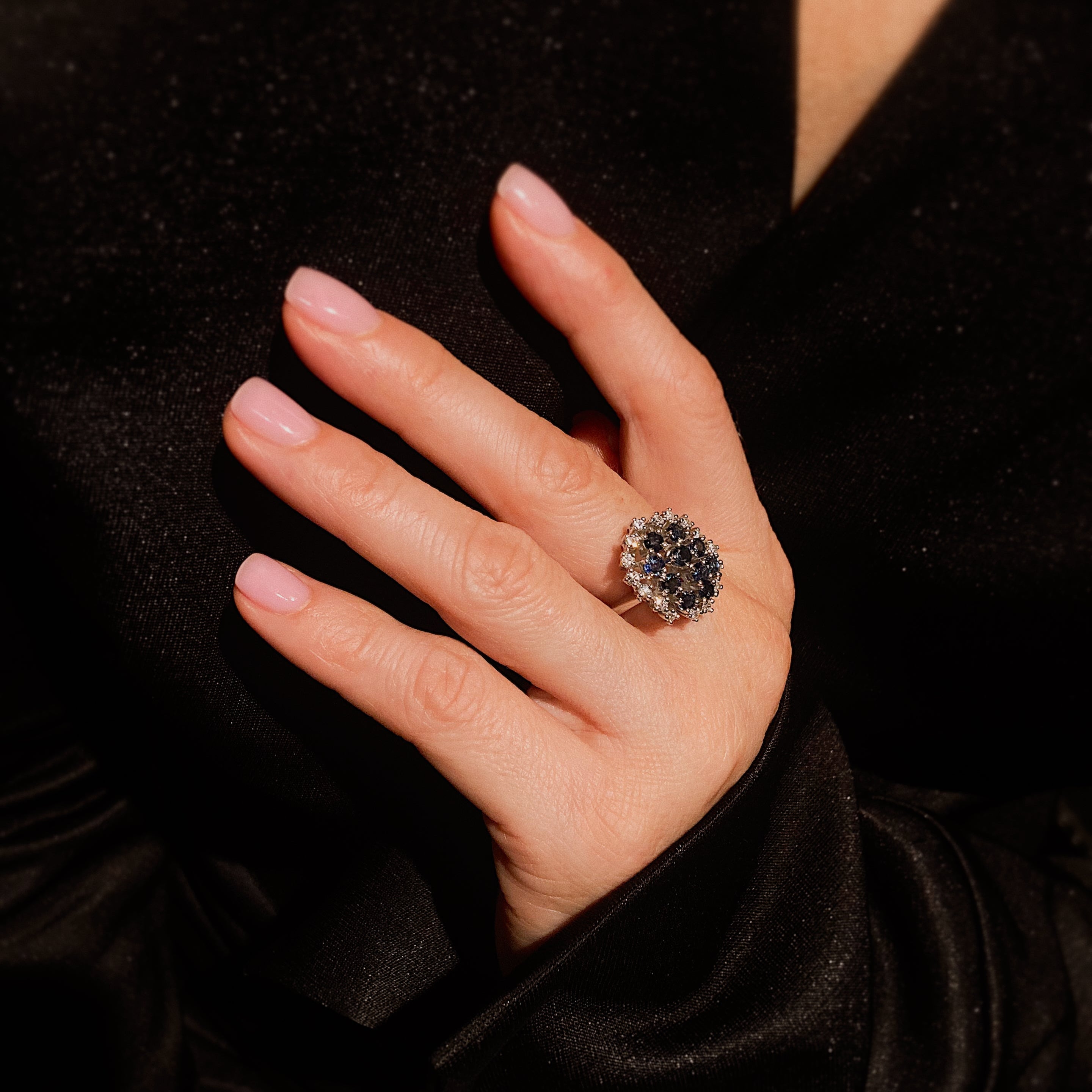 Woman model's hand wearing the contemporary vintage white gold cluster cocktail ring with blue sapphires and diamonds.